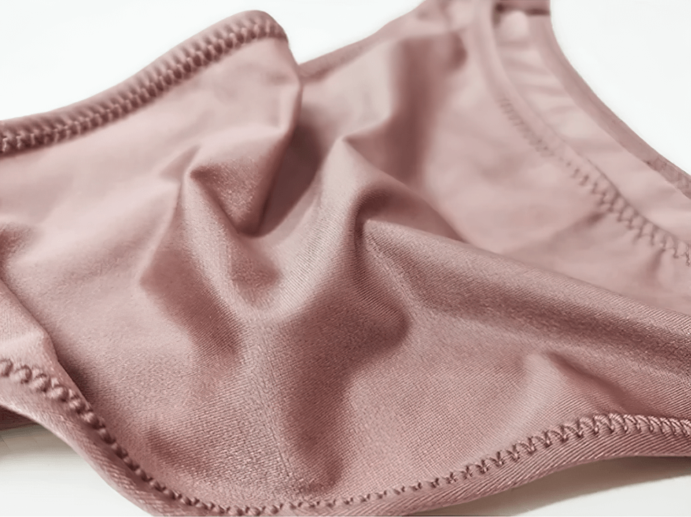 Close-up of pink low-rise G-string panties with knit design and solid pattern, showcasing sleek polyester and nylon blend fabric.